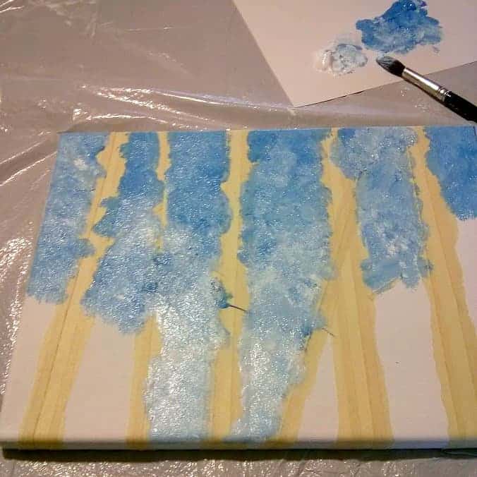 Dabbing blue sky paint on canvas with taped off tree shapes