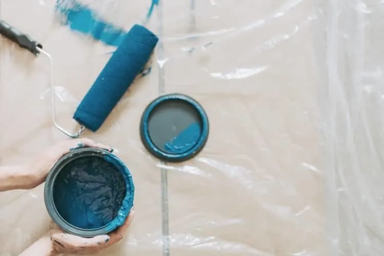 Open blue paint can with roller on tarp