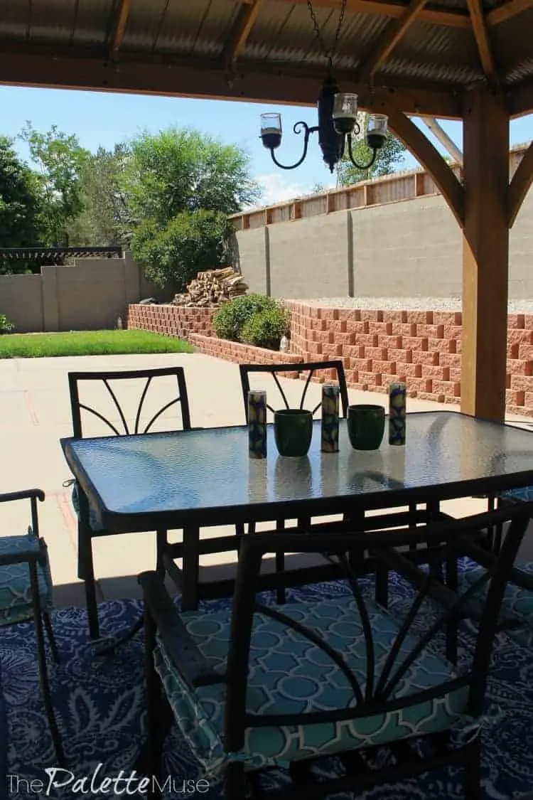 A gazebo and shaded dining set against a background of painted concrete wall.
