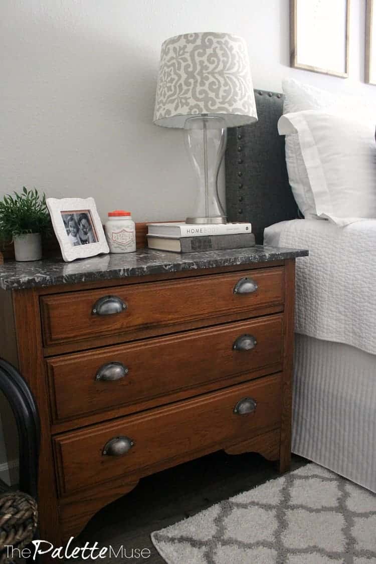 Wood dresser with gray marble top serves as nightstand next to the bed.