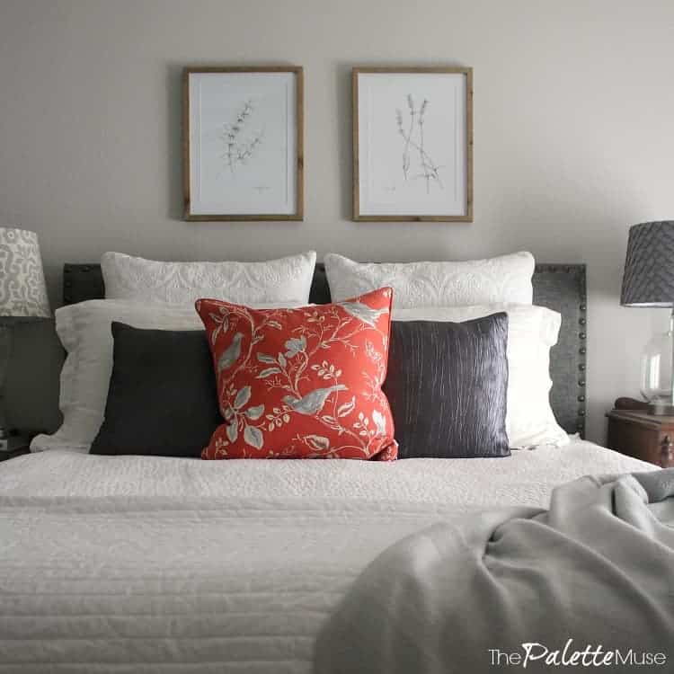 Bed with white and gray bedding, on gray wall with botanical drawings.