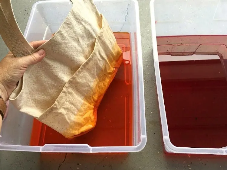 Dip-dying a tote bag by dipping it in orange dye, then red dye.