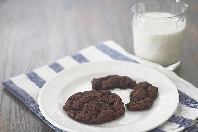 Dark chocolate cookies on a plate with a glass of milk in the background