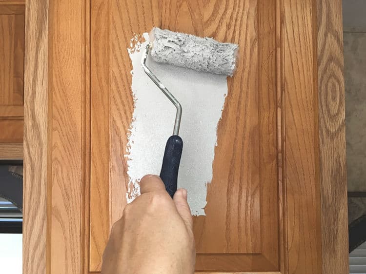 Painting the first stroke of light gray paint on laminate cabinets