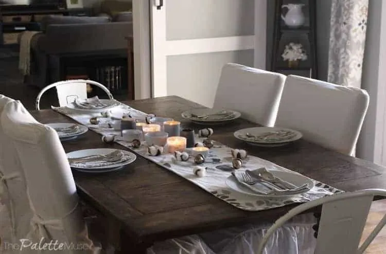 Dark wood table with white chairs, table runner, and dishes.