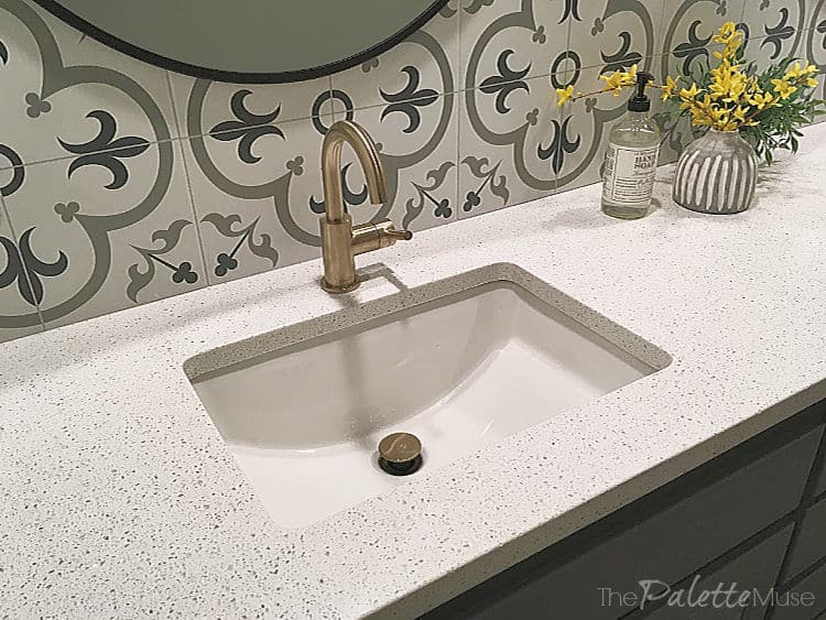 Brass sink faucet in front of patterned tile backsplash