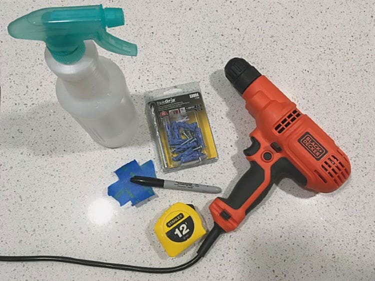 Supplies for drilling into a tile backsplash to hang mirrors. You'll need a drill, a masonry bit and masonry anchors, a spray bottle with water, and tools for marking the spot.