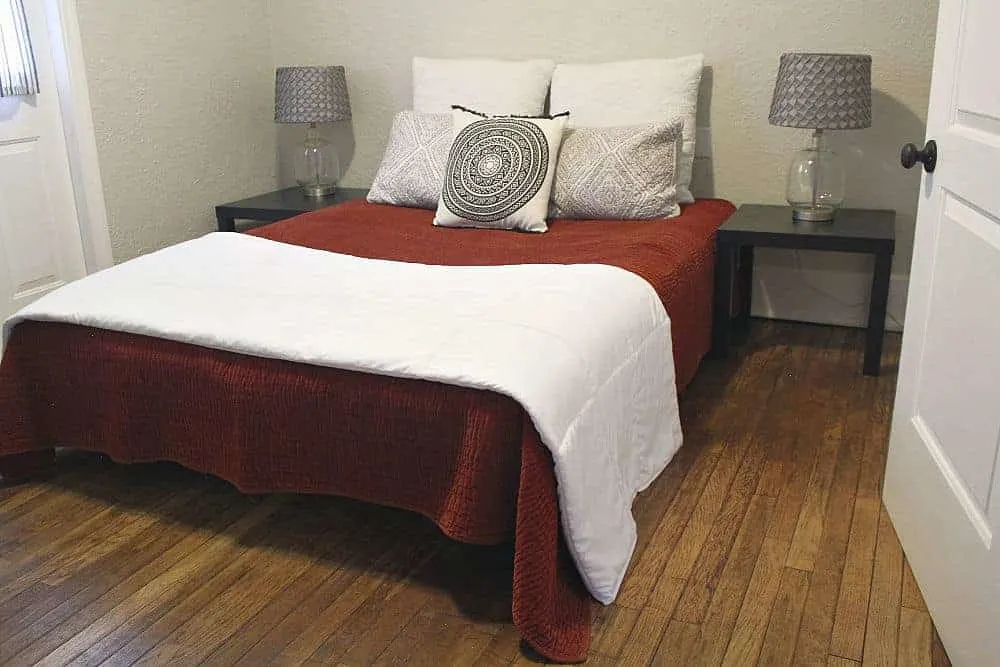Queen bed with white covers and warm hardwood floors.