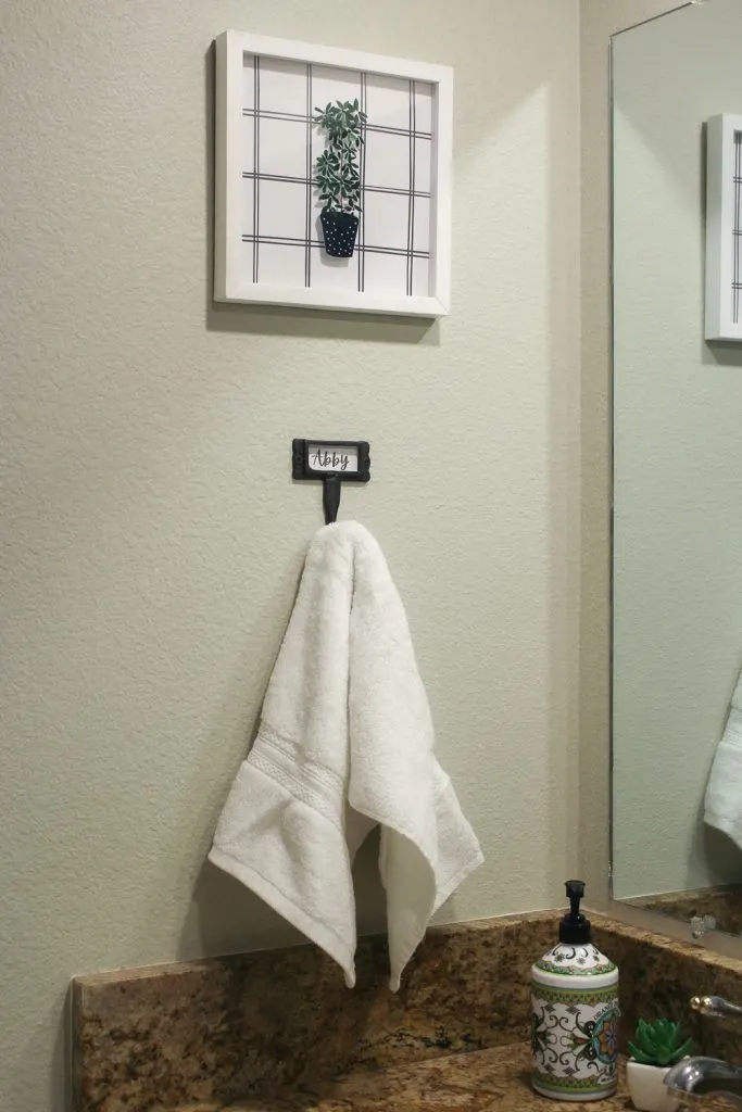 White framed print of potted plant hanging over white hand towel in girls bathroom