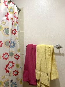 pink and yellow towels hang in a bunch on a towel rack next to a floral shower curtain in girls' bathroom