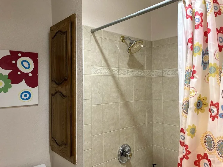Brown cabinet next to beige shower with red flower shower curtain.