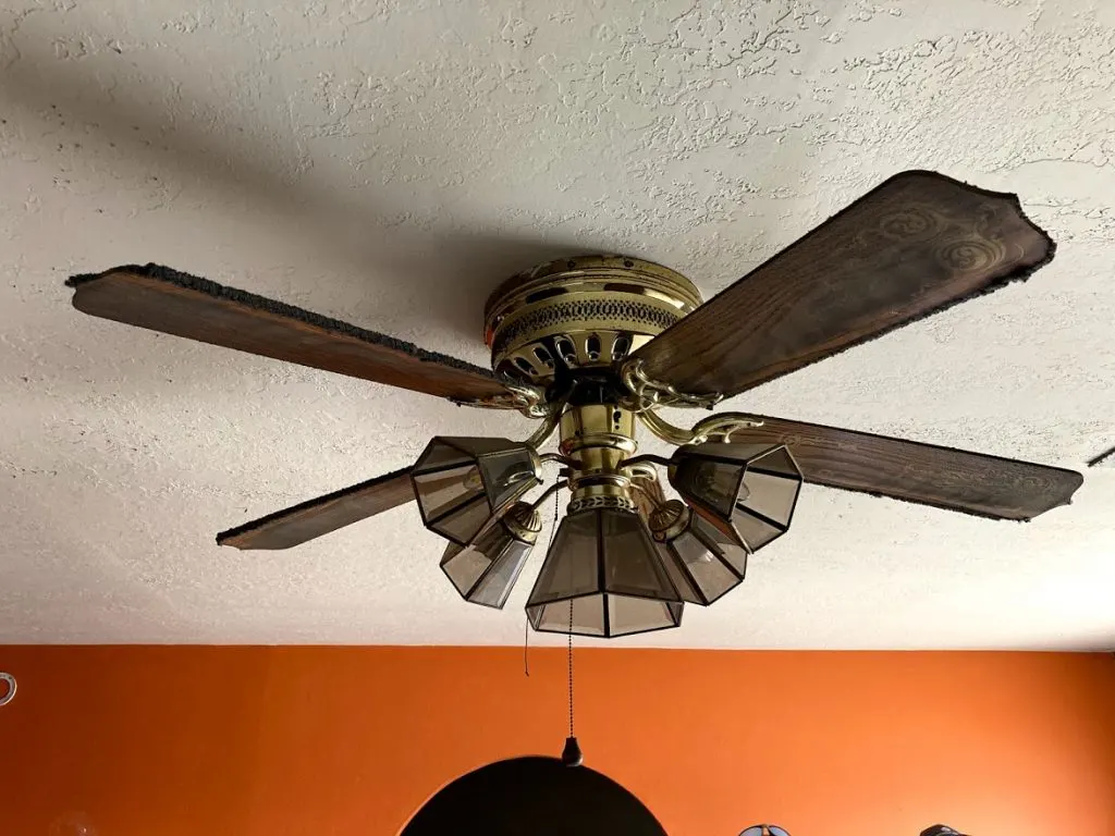 Dated ceiling fan with years of dirt built up on the blades, against a dark orange wall