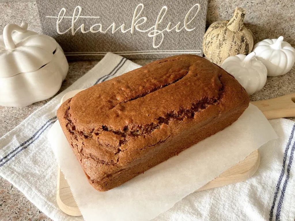 Pumpkin bread on a bread board in front of a sign that says thankful.
