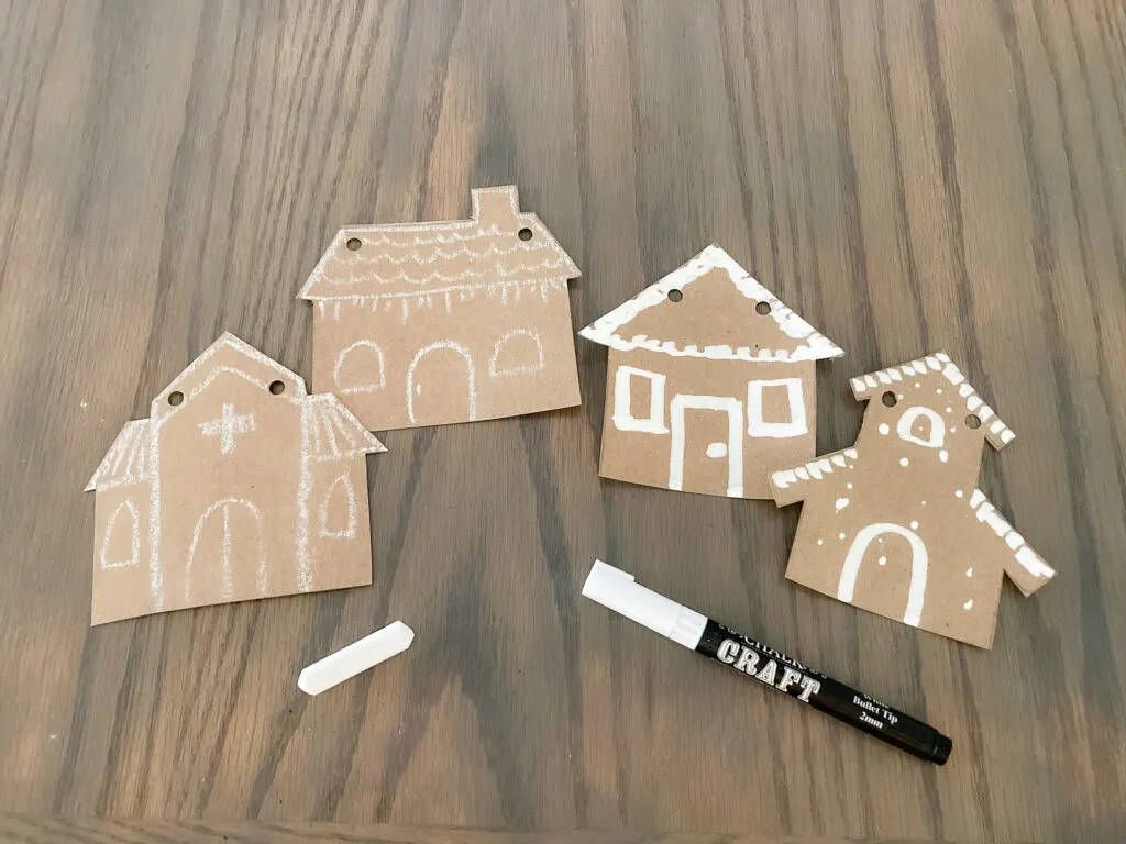 Paper gingerbread house shapes decorated with white chalk and white chalk marker.