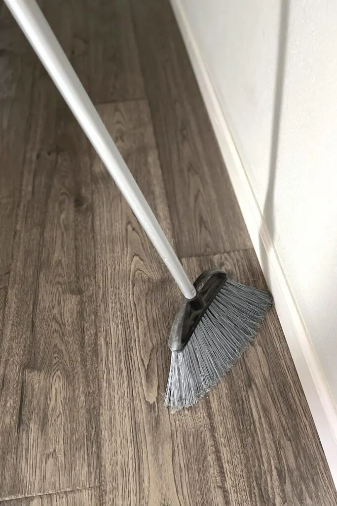 A broom sweeping along a white baseboard.