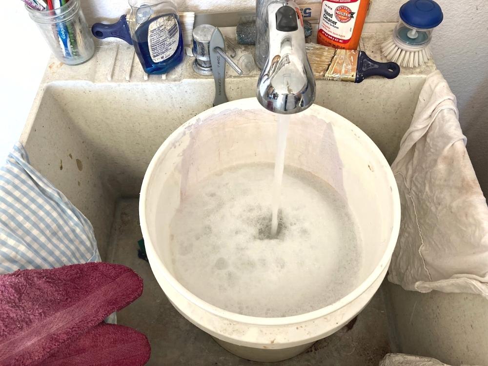 A large bucket in a laundry sink, being filled with water