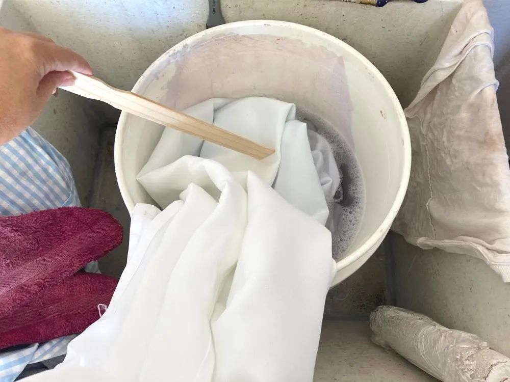 Stirring white fabric in a large bucket to remove dye