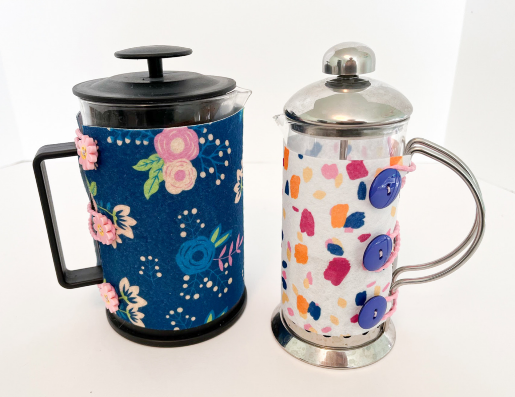 Two French presses with coordinating blue and pink cozies, or covers.