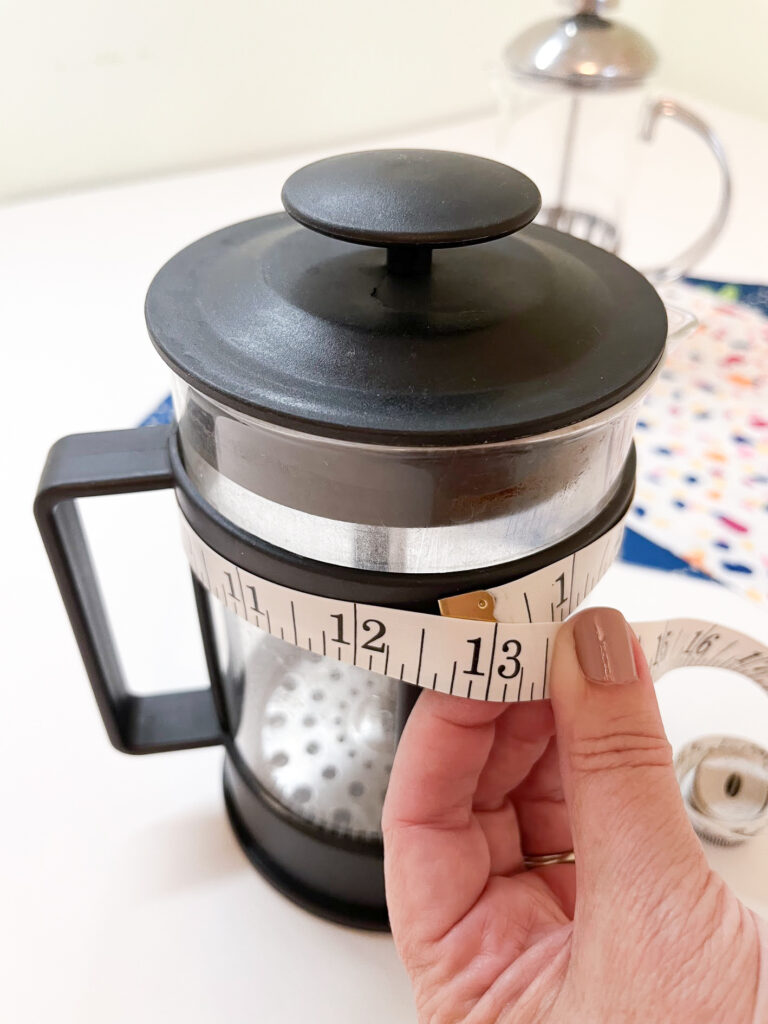 Measuring the width of a French press with a tape measure.