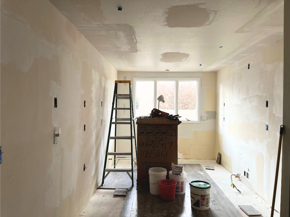Empty room with patched drywall and a ladder and buckets. Before starting a kitchen remodel, decide how much of the work will be hired out to the pros.