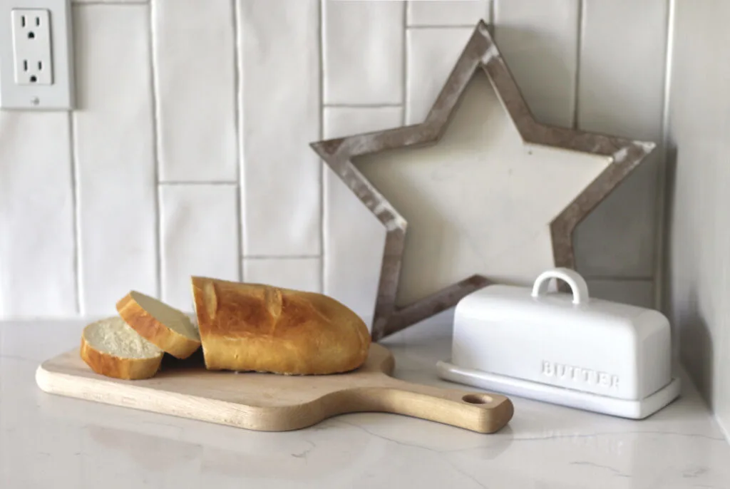 White kitchen countertop with a butter dish and sliced french bread on bread board.