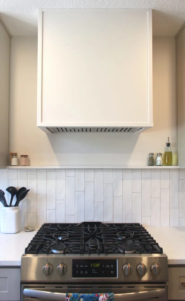 stainless steel oven with minimalist hood range above a white backsplash