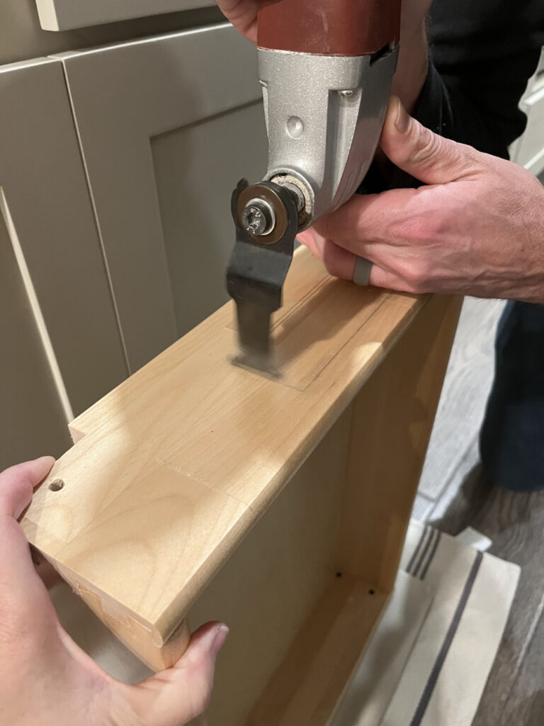 Using an oscillating saw to cut a rectangular hole in the back of a drawer to fit a charging cable.