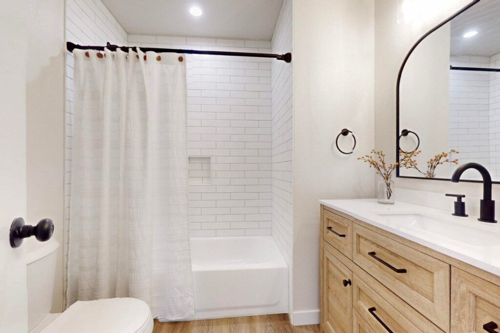 A bright updated bathroom with white subway tile and a wooden vanity with black fixtures.