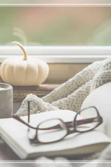 Thoughts on empty nesting, represented by a book, glasses, a candle, and a small white pumpkin.