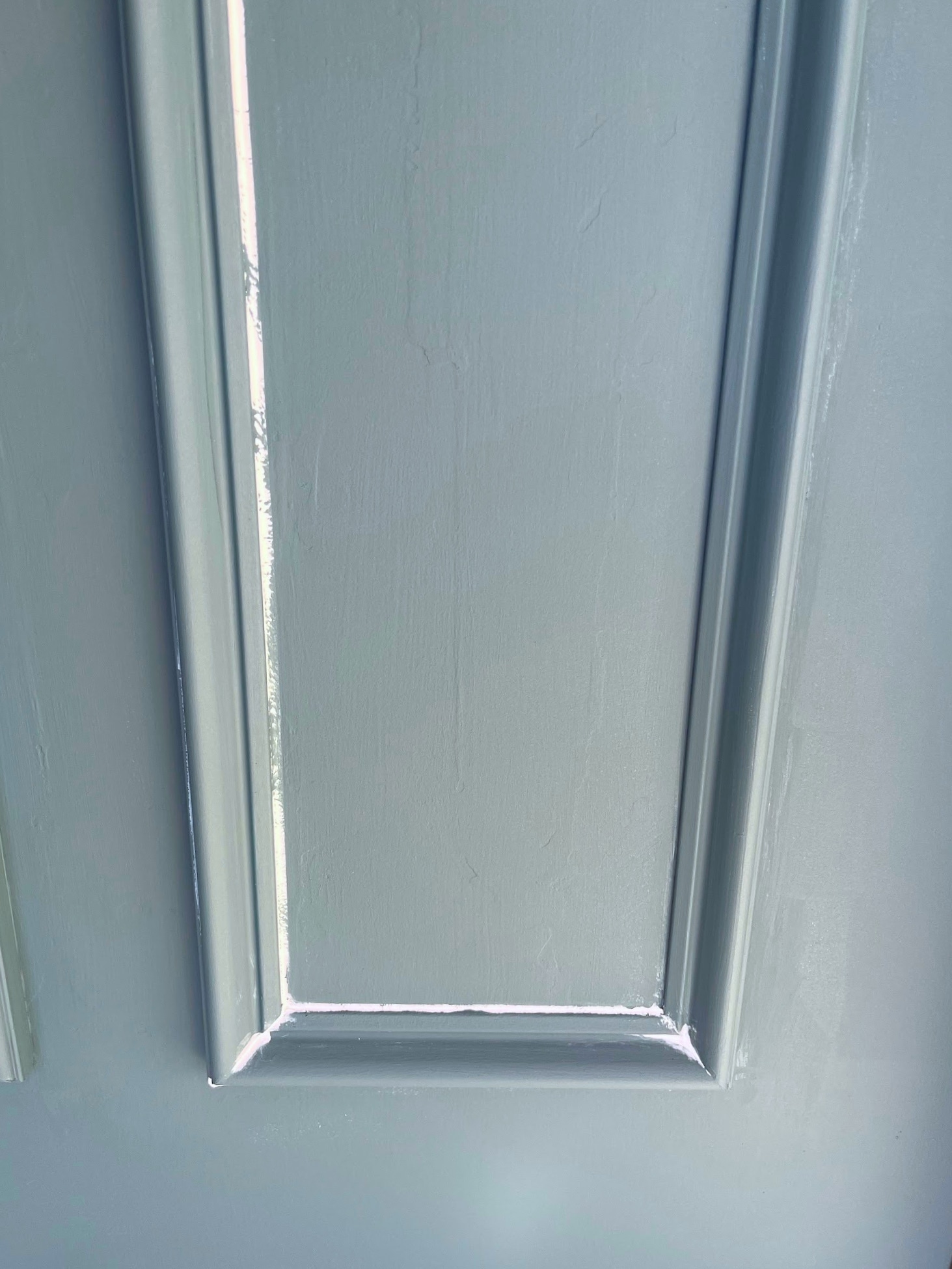 A closeup of white caulk in the corners of molding on a blue door.