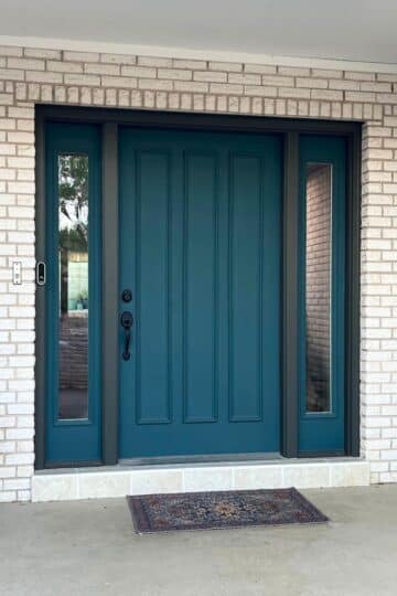 A dark teal front door with black trim and hardware, and full sidelights.