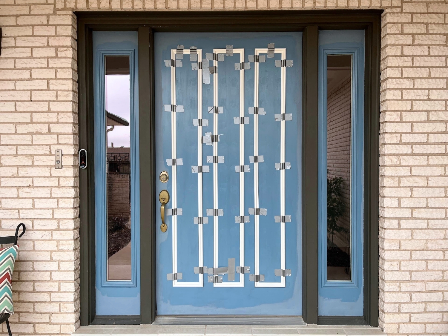 White molding pieces are duct taped to a blue front door while their adhesive dries.