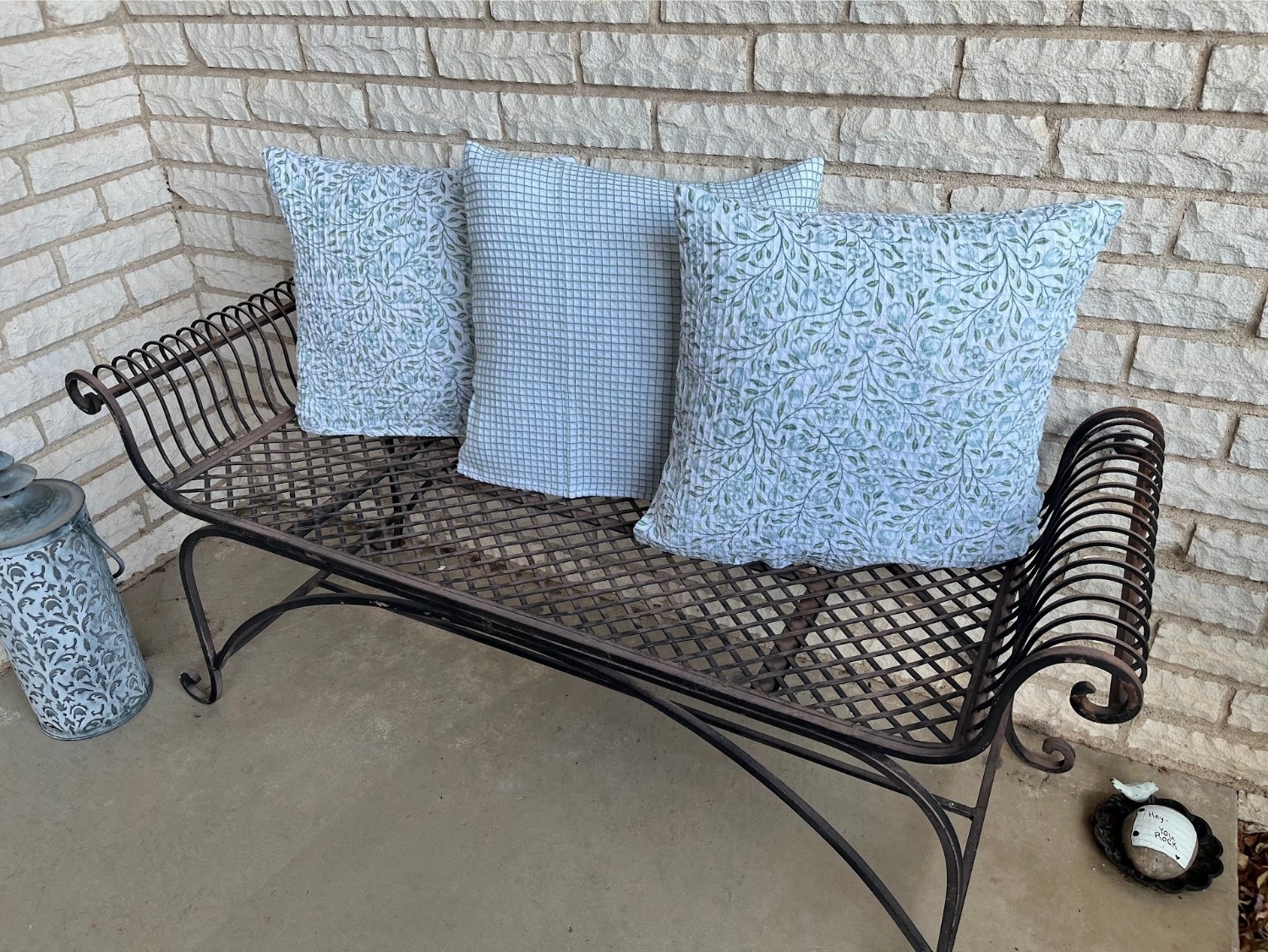 Three blue and green throw pillows lined up on a wrought iron bench.