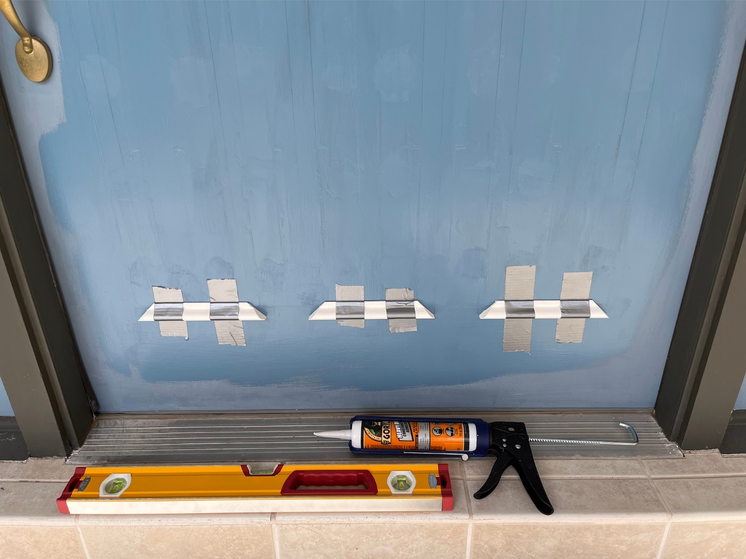 A blue front door with white molding pieces taped to it, with gorilla glue and a level laying in front.