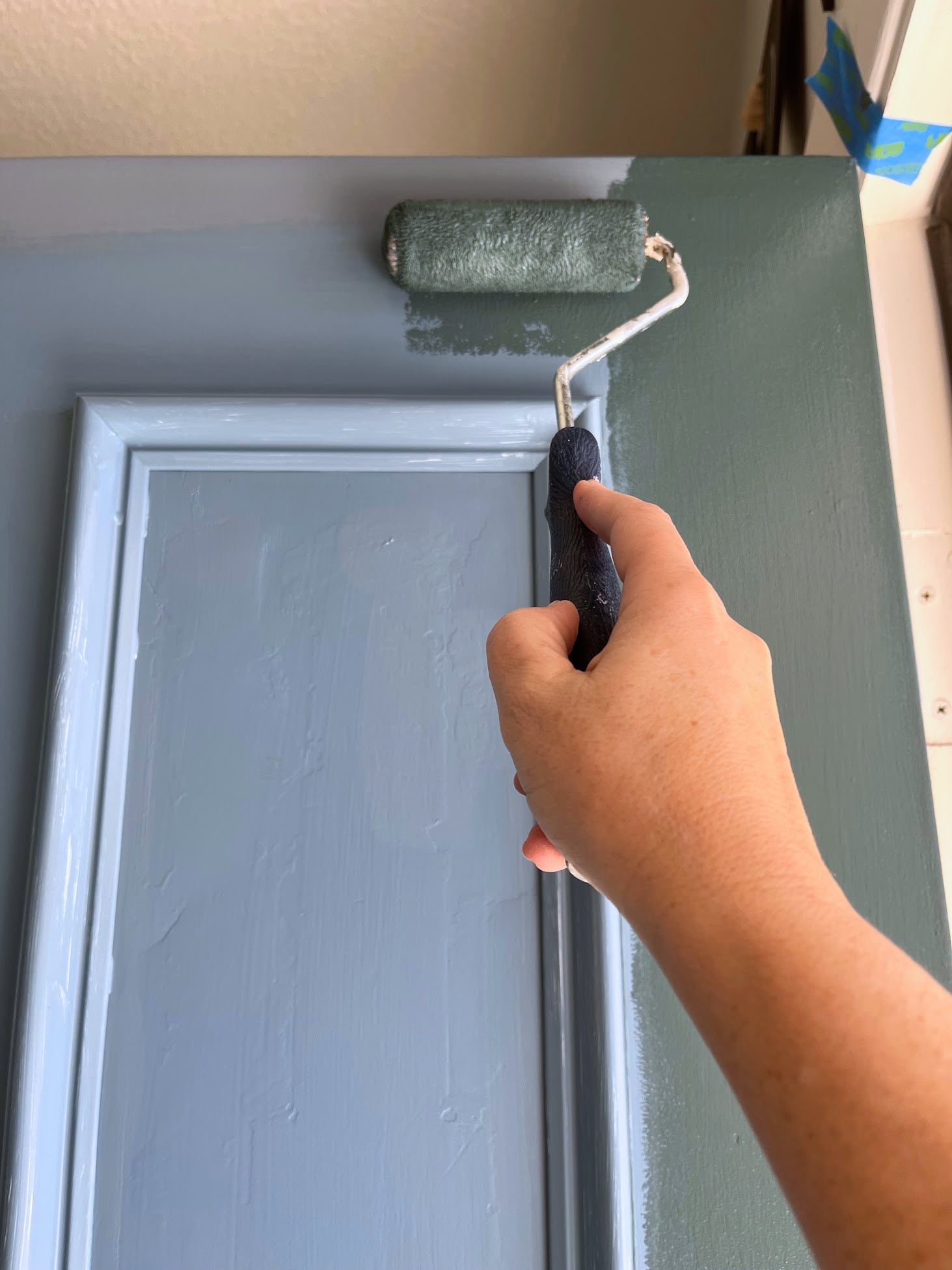 Using a roller to paint teal over a blue door.