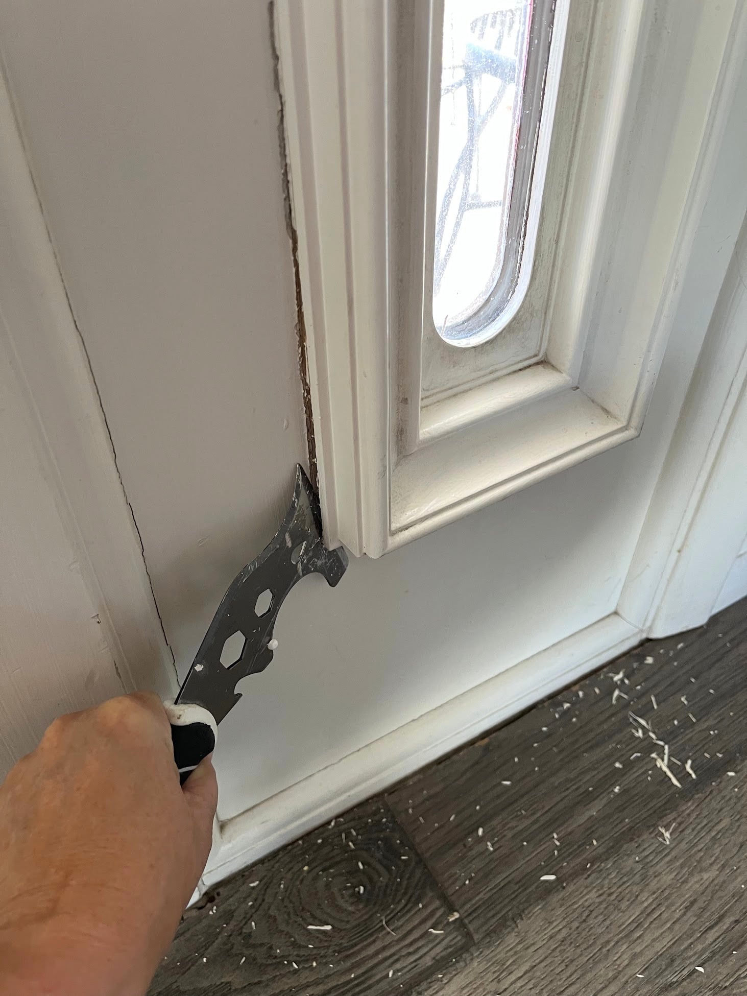 Using a painter's tool to score and pry the molding from a door sidelight.