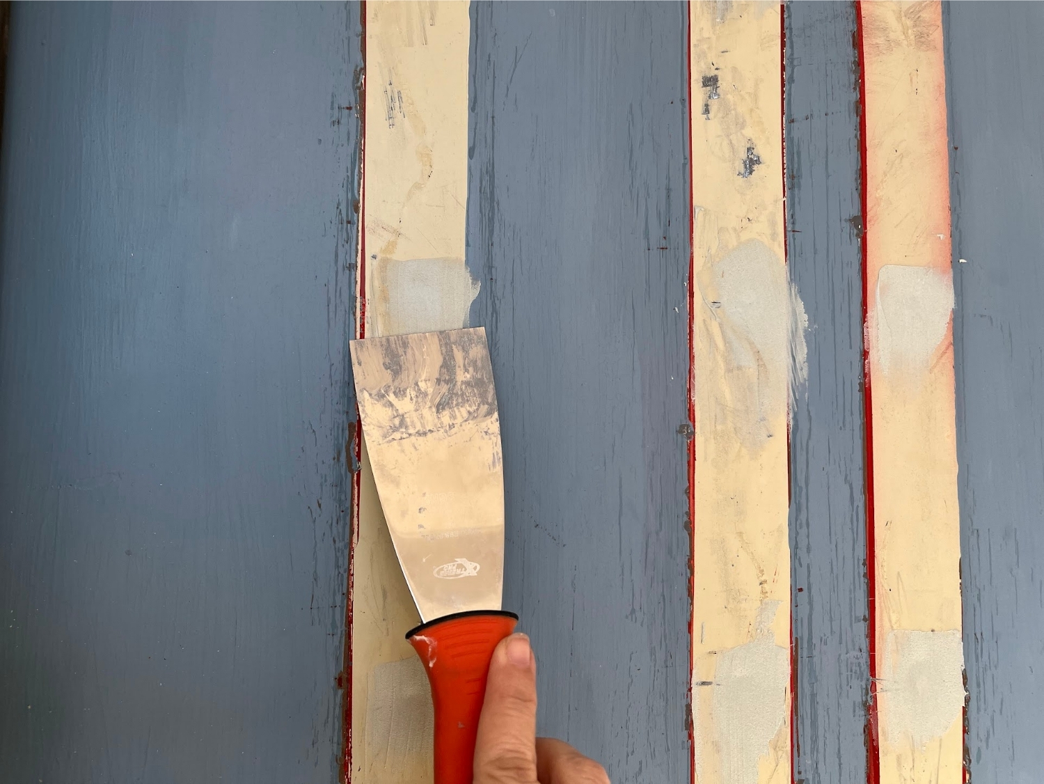 Using a putty knife to apply Bondo to nail holes in a front door.